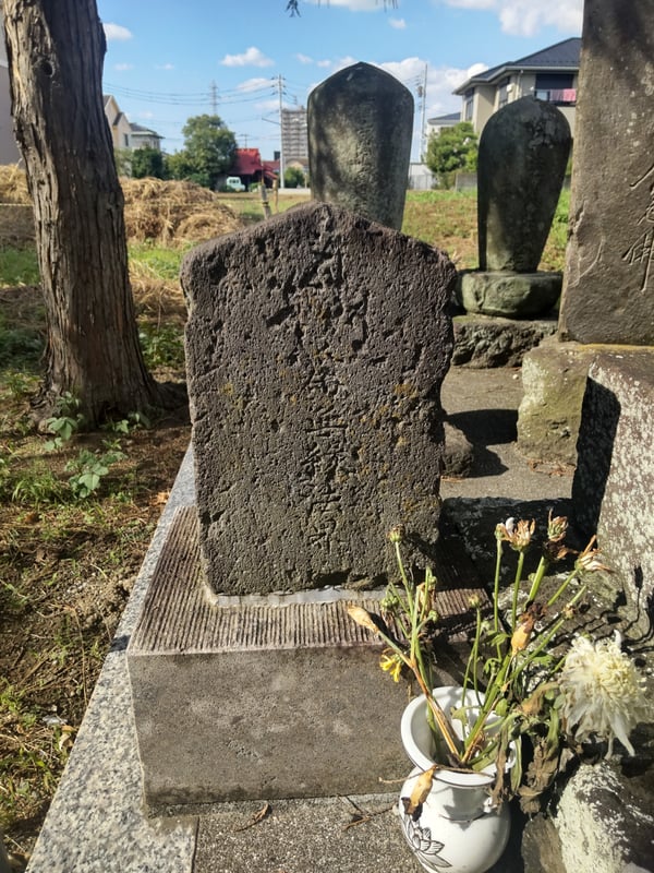 The image shows a stone monument inscribed with "オチョバンバ供養塔," standing outdoors.