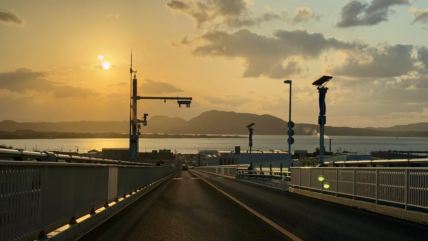 A person is gazing into the distance from atop a long bridge at dusk.
