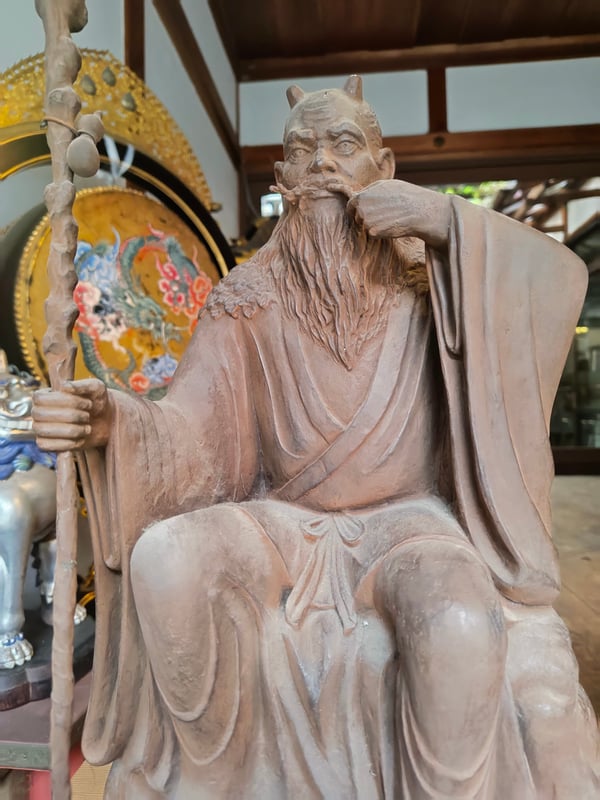 A statue of Shennong stands vividly against a green backdrop, depicting the ancient agricultural deity's features.